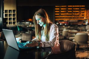 Focused female developer sitting in a dark coffee shop and finishing tasks